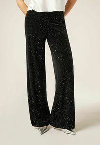 Velvet zwarte wijde broek met zilveren sprankels door het geheel, met een hoge taille en een soepele textuur. Gecombineerd met zilveren spitse hakken.