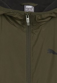 Juoda žalia zip-up striukė su aukštu apykakle, sidabrine užtrauktuku ir juodu Puma logotipu. Lygus, lengvas audinys su subtiliu blizgesiu.