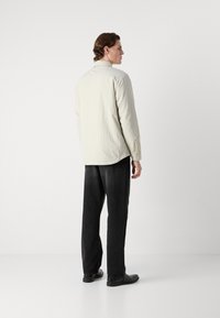 Light beige, long-sleeve shirt with a straight cut and back yoke. Paired with black, straight-leg trousers and black loafers.