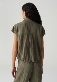 Olivengroene blouse met korte mouwen, met een losse pasvorm en afgeronde zoom, gemaakt van lichtgewicht, gekreukt stof. De achterkant heeft een gestikte detail.