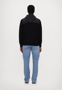 Pulover cu capuz negru, cu un panou gri la umeri, asociat cu blugi drepți de un albastru deschis și adidași albi. Design simplu.