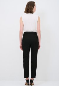 Witte mouwloze top gecombineerd met hoge zwarte broeken. De broeken zijn slim-fit met een gladde textuur en een subtiele achterzak. Zwarte hakken.