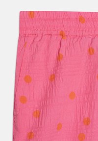 Rosa stoff med en rynket tekstur, prydet med store oransje prikker. Elastisk midjeopplegg øverst med horisontale sømmer.