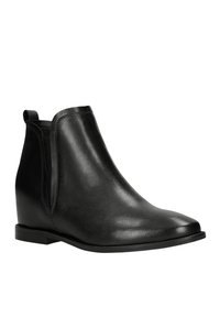 Stivali alla caviglia in pelle nera con tacco a zeppa, dotati di pannelli laterali elasticizzati, punta arrotondata e una texture liscia. Design minimalista.