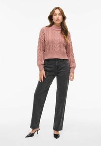 Roza pletena jopica z visokim ovratnikom, ki ima dizajn kablovskega pletenja. V kombinaciji z visokim pasom temno sivih kavbojkah in črnimi petastimi mule čevlji.