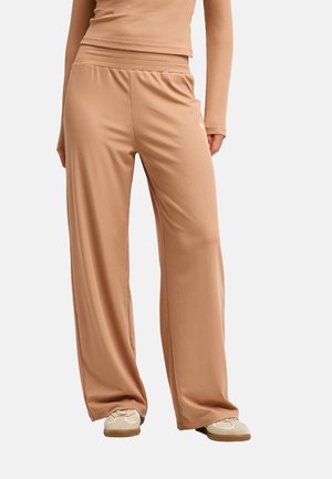 Personne portant un pantalon large côtelé beige et un haut à manches longues assorti avec des baskets beige sur un fond uni.