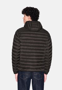 Giacca a vento imbottita scura con design trapuntato, cappuccio e polsini a coste. Il materiale sembra liscio e leggero, con una silhouette aderente.