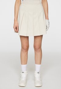 Gonna plissettata color crema con vita attillata, realizzata in tessuto leggero. Abbinata a sneakers bianche alte e calzini alla caviglia.