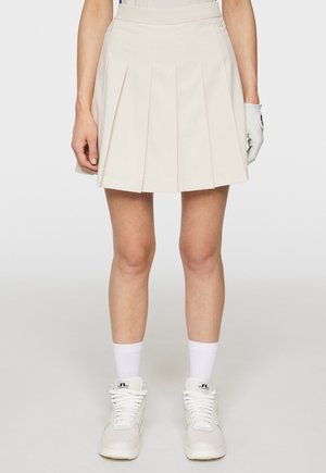 Cream pleated skirt with a fitted waist, made from lightweight fabric. Paired with white high-top sneakers and ankle socks.