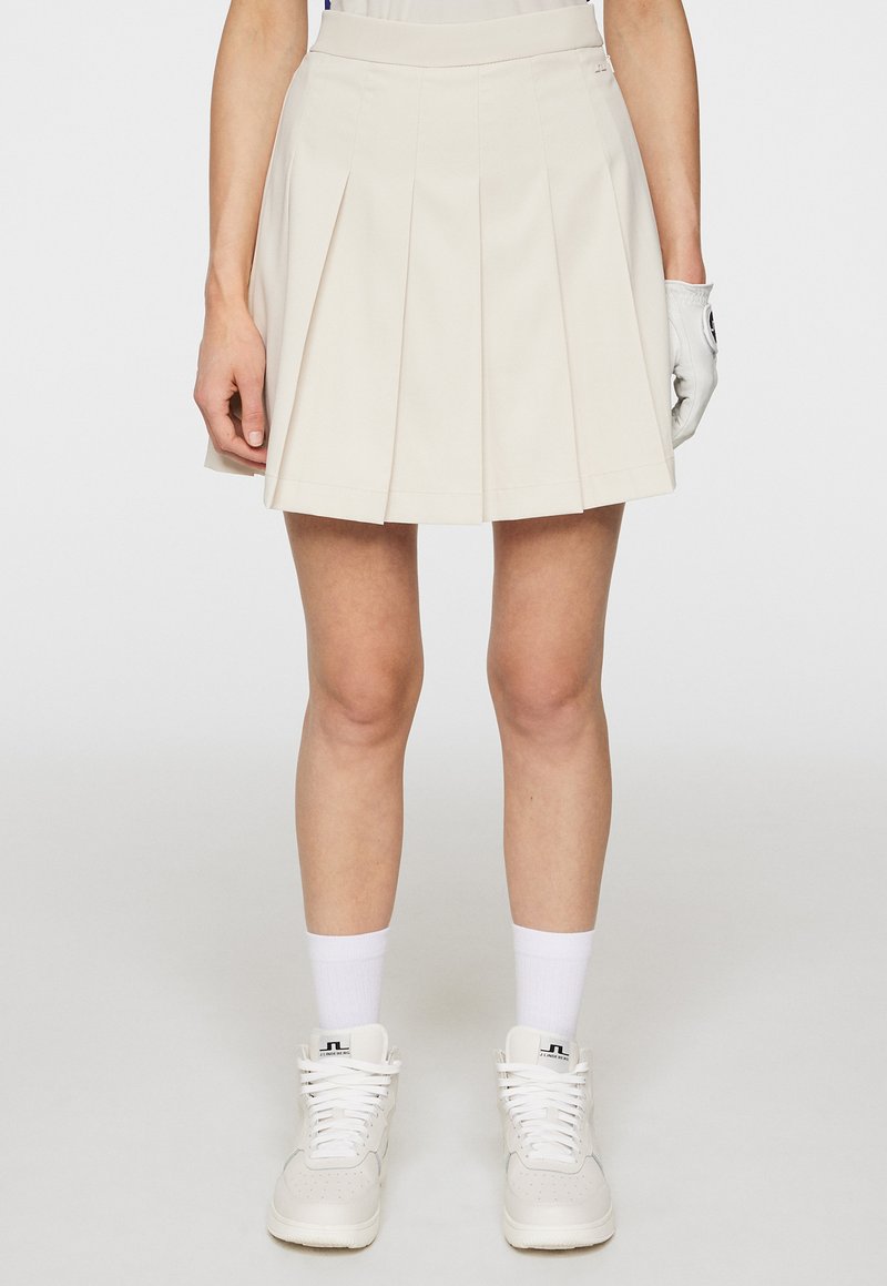 Gonna plissettata color crema con vita attillata, realizzata in tessuto leggero. Abbinata a sneakers bianche alte e calzini alla caviglia.