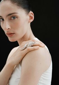 Anillo plateado en forma de cocodrilo con un detallado intrincado, que presenta escamas texturizadas, posado sobre el hombro de un modelo que lleva una blusa blanca minimalista.