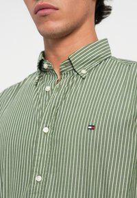 Groen en wit gestreept overhemd met knopen, voorzien van een klassieke kraag, textuurstof en een klein logo-embleem op de borst.