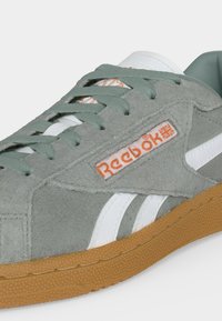 Сив велурен маратон на Reebok със зелени връзки, бели лого ивици, оранжев текст Reebok и текстурирана кафява гумена подметка.
