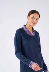 Pull en marine à manches longues avec un col et des poignets à motifs floraux. Texture douce, col rond et design décontracté.