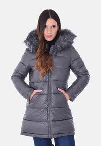 Cappotto imbottito grigio con cappuccio foderato in pelliccia, caratterizzato da un design di lunghezza media, chiusura con zip frontale e tasche laterali con zip. Tessuto trapuntato testurizzato.