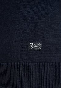 Dark blue knitted fabric with a small rectangular patch labeled "Petrol Ind. Crude Oil REF. 5026.SE" stitched near the bottom.