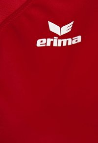 Tissu rouge avec le logo blanc de la marque "erima" et des ailes stylisées imprimées près de la couture.