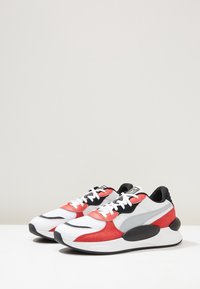 Red, white, and gray athletic shoes with a mix of mesh and suede, featuring black accents, rounded sole, and contrasting laces.