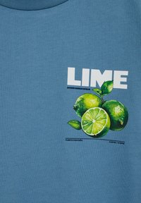 Plava majica sa slikom tri zelena limeta, jedna narezana, i riječju "LIME" velikim bijelim slovima iznad voća.