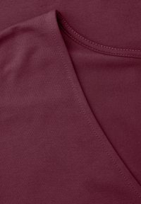 Gros plan sur un tissu bordeaux montrant une encolure en V et des détails de couture visibles sur un textile doux et lisse.