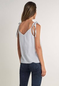 Top senza maniche a righe in bianco e blu navy, con un design a V sulla schiena e spalline annodate. Indossato sopra jeans scuri.