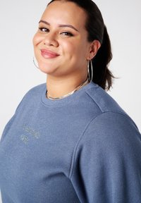 Blauwe, lange mouwen sweatshirt met een subtiele glans, met een ronde halslijn en 'LE PRODUIT' print in zilver op de voorkant.