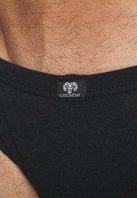 Sous-vêtements en coton noir avec une texture lisse, ornés d'une étiquette avec un logo de bélier et le nom de la marque "ceceba" sur la taille.
