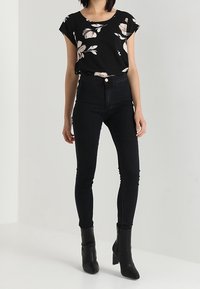 Blusa negra con flores, de mangas cortas, combinada con unos jeans skinny negros de cintura alta y botas negras de tobillo. Tejido suave, diseño casual.