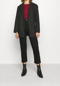 Blazer grigio oversize, camicia burgundy, jeans neri a vita alta e stivaletti neri. Tessuto morbido, vestibilità su misura e design della punta affusolata.