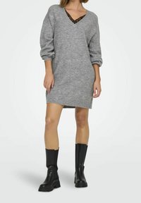 Robe en tricot gris avec un décolleté en V et des manches bouffantes, associée à un débardeur en dentelle noire en dessous et des bottes noires jusqu'au genou.