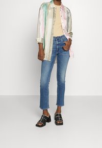 Camisa de botones a rayas coloridas sobre una blusa beige, combinada con jeans ajustados azules y sandalias negras de tacón cuadrado.