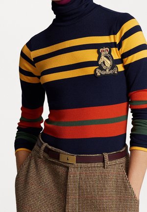 Marineblauwe coltrui met gele, rode en groene horizontale strepen en een crest-patch, gecombineerd met bruine geruite broek en een bruine riem.
