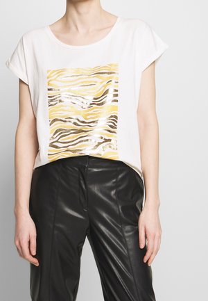 Biały krótki top z krótkim rękawem ozdobiony złotymi i brązowymi paskami zebry, w połączeniu z czarnymi, wysokim stanem spodniami ze sztucznej skóry.