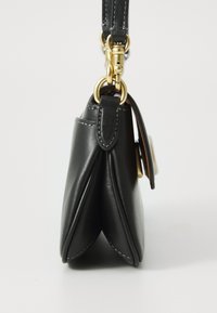 Μαύρη δερμάτινη γυναικεία τσάντα πλευρική θέα με χρυσούς μεταλλικούς κρίκους και κούμπωμα, μαύρο ιμάντα προσαρτημένο και ορατές ραφές.