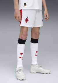 Weiße Fußballshorts mit roten Akzenten und Logo; kombiniert mit weißen Socken mit einem roten Design; abgerundet mit silbernen Footballschuhen.