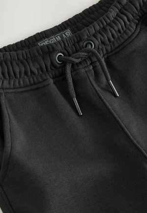 Pantaloni de trening negri din bumbac, cu talie elastică, șnur ajustabil și cusături plate. Eticheta spune "REGULAR."