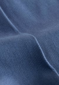 Gros plan sur un tissu bleu texturé avec un motif de tricotage petit et uniforme, et de légers plis créant des ombres courbes.