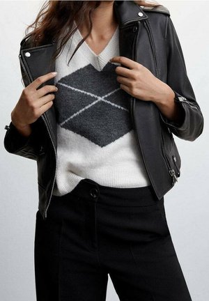 Giacca di pelle nera sopra un maglione bianco con motivo a rombi grigi, abbinata a pantaloni neri. Focus su trame e contrasto.