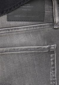 Tela de mezclilla gris con una textura suave, con costuras cosidas, una etiqueta de cuero con texto en relieve y un diseño minimalista.