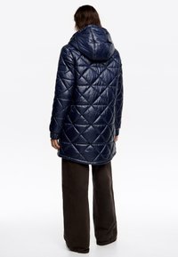 Námornícky modrý prešívaný zateplený kabát s veľkou kapucňou, s lesklým povrchom, elastickými manžetami a dĺžkou po kolená pre zahriatie.