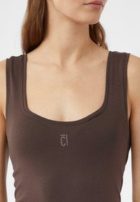 Braunes, figurbetontes Tanktop mit weitem Rundhalsausschnitt, aus weichem Material gefertigt. Verfügt über ein dezentes Logo auf der linken Vorderseite.