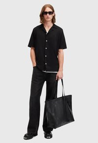 Black short-sleeve shirt with white buttons, black wide-leg jeans, black boots, and a large black tote bag with subtle embossed pattern.