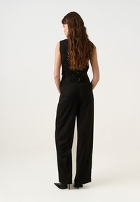 Juoda be rankovių šokinė su prigludusia liemeniu, plačiomis kelnėmis ir diržo akcentais. Pagaminta iš sklandžios medžiagos, demonstruojanti švarų, modernų dizainą.