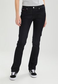 Vaqueros skinnies de mezclilla negra con una cintura de altura media, que presentan un clásico diseño de cinco bolsillos y herrajes plateados, combinados con zapatillas negras.