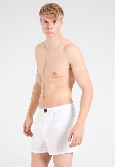 Witte katoenen boxershorts met een elastische tailleband, voorzien van een klein blauw etiket aan de voorkant. Gladde textuur en een relaxte pasvorm.