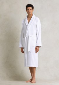 Accappatoio in spugna bianca con maniche lunghe, design avvolgente, tasche laterali e cintura coordinata. Presenta un piccolo logo ricamato sul petto.