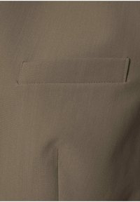 Zbliżenie beżowej kieszeni z poziomym cięciem i widocznym przeszyciem na gładkim, teksturowanym materiale.