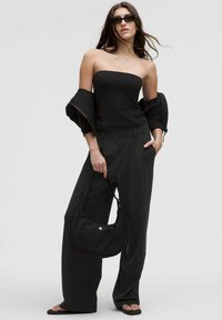 Top nero senza spalline, pantaloni neri a gamba larga e una borsa a spalla nera abbinata. Tessuto testurizzato, design minimale e occhiali da sole eleganti.