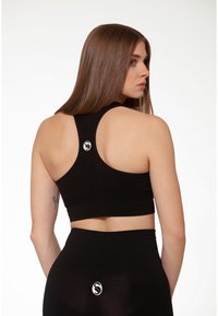 Sostenitore sportivo nero con design a schiena scoperta, realizzato in un tessuto liscio. Presenta un piccolo logo sul retro, abbinato a leggins a vita alta.