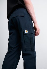 Granatowe spodnie cargo wykonane z trwałego materiału z wieloma kieszeniami, z prostokątną naszywką-logo na lewym udzie i prostym krojem.